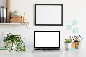 Laptop and poster frame on white wall in stylish home office. Mock up.