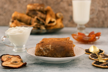 A portion of homemade pancakes with filling. Apricot jam. Sour cream in sauceboat. Dry pear and lemon slices.