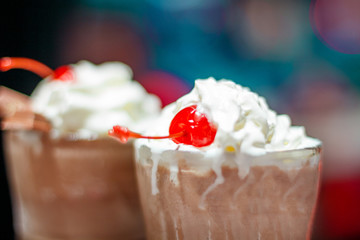 two glasses with a milky neck with a cherry against the window