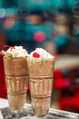 two glasses with a milky neck with a cherry against the window