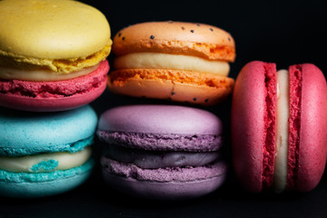 Pile of sweet colourful macaroons on black background.