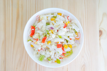 Salad with corn and crab sticks in white dish on wooden background top view