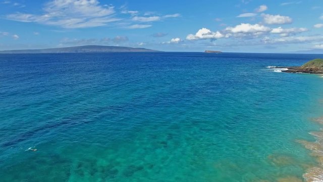 Panning aerial shot of a Snorkler in Maui Hawaii in beautiful blue water with sandy beach and land in background