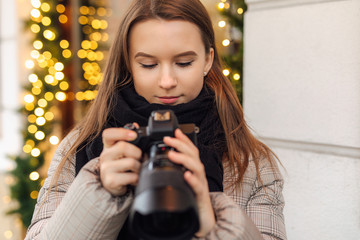 Photographer girl walk in the street and take photos in camera with happy face. Wear black scarf. Winter, autumn outfit.