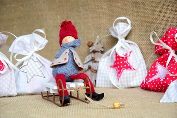 Wichtlein auf einem weißen Schlitten mit Geschenksäckchen aus Stoff