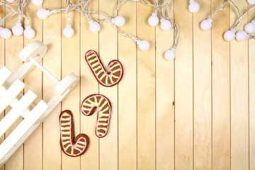 Tło - życzenia świąteczne - Boże Narodzenie - białe sanki i kolorowe pierniki z lampkami na jasnym tle - obrazy, fototapety, plakaty