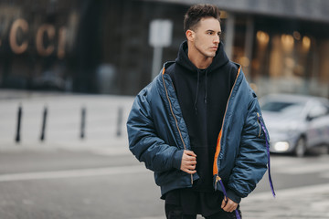 Fashionable man walk on the street near buildings. Wear blue jacket and all black. Winter, autumn...