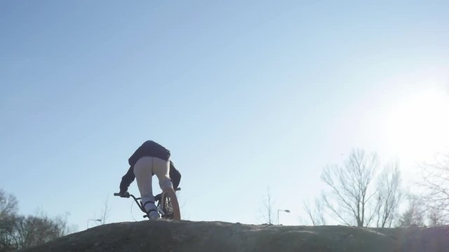 slowmotion of a bmx kid on a dusty track jump on a bumb with a nice sun flare from the side