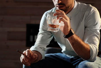 Man with glass of whiskey and cigar at home, closeup. Space for text