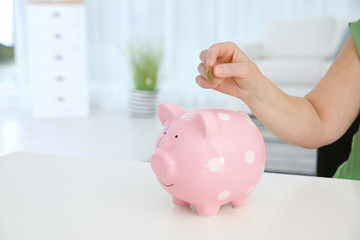 Mature woman putting money into piggy bank at table, closeup. Space for text