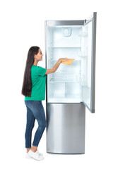 Young woman cleaning refrigerator with rag on white background