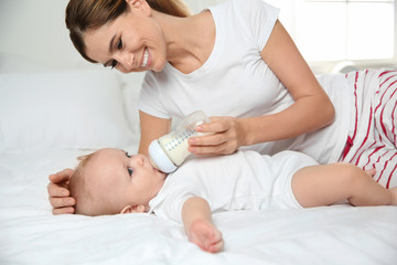 Lovely mother feeding her baby from bottle on bed at home