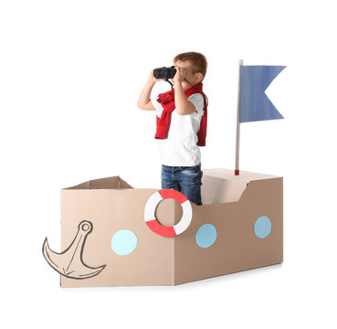 Cute little boy playing with cardboard ship on white background