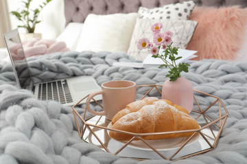 Tray with tasty breakfast and laptop on bed