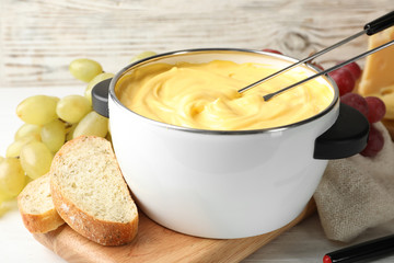 Pot with delicious cheese fondue and forks on wooden table
