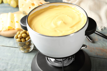 Pot with delicious cheese fondue on wooden table