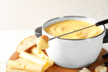 Pot of delicious cheese fondue and fork with bread on table
