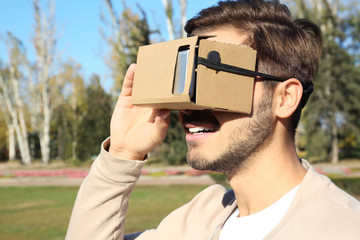 Young man using cardboard virtual reality headset outdoors