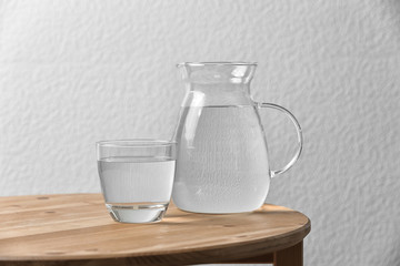 Pitcher and glass with water on table near white wall