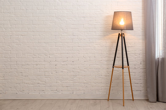 Modern floor lamp against brick wall indoors. Space for text