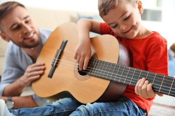 Father teaching his little son to play guitar at home