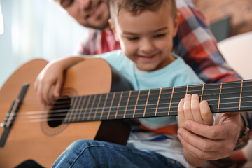 Father teaching his little son to play guitar at home