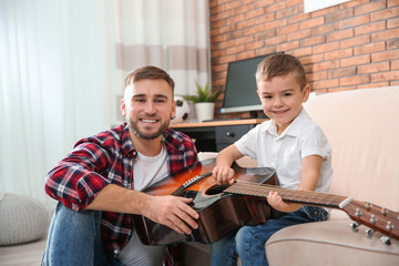 Fototapeta premium Father teaching his little son to play guitar at home