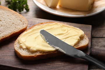 Spreading butter onto toast with knife on wooden board - obrazy, fototapety, plakaty