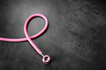 Pink stethoscope as awareness ribbon on dark background, space for text. Breast cancer concept