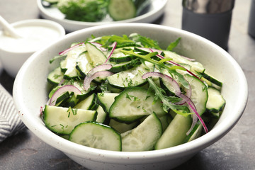 Delicious cucumber salad with onion and arugula in bowl on grey table, closeup