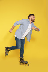 Young man with inline roller skates on color background