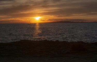 Seascape with sailboat over sunset