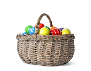 Decorated Easter eggs in wicker basket on white background