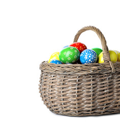 Decorated Easter eggs in wicker basket on white background