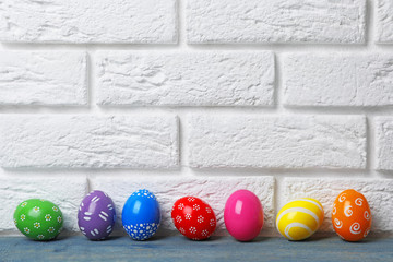Decorated Easter eggs on table near brick wall. Space for text