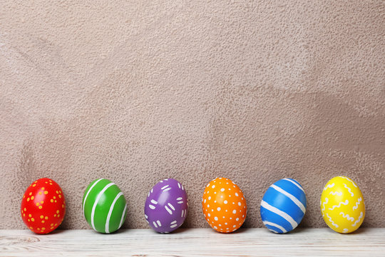 Decorated Easter eggs on table near color wall. Space for text