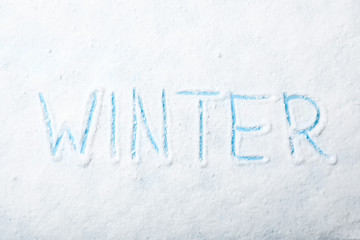 Word WINTER written in snow on color background, top view