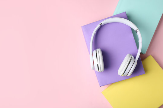 Modern headphones with hardcover books on color background, top view. Space for text