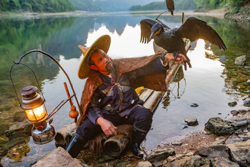 Chinese cormorant fisherman on raft in lake holding a black cormorant bird in Guilin, China.