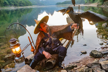 Chinese cormorant fisherman on raft in lake holding a black cormorant bird in Guilin, China.