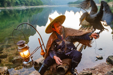 Chinese cormorant fisherman on raft in lake holding a black cormorant bird in Guilin, China.