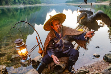Chinese cormorant fisherman on raft in lake holding a black cormorant bird in Guilin, China.
