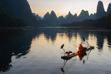 Cormorant fisherman on raft in lake in Guilin, China, with three cormorant birds. Fisherman is...