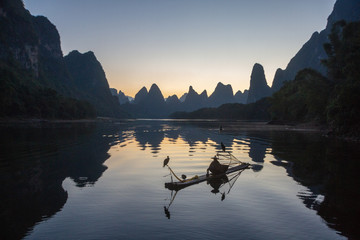 Cormorant fisherman on raft in lake in Guilin, China, with three cormorant birds. Fisherman is...