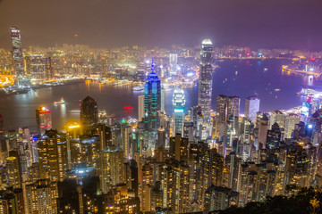 Hong Kong skyline at night as seen from Victoria Peak. Illuminated skyscrapers in foreground, Hong Kong harbor in background.