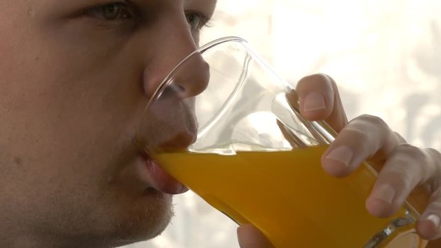 Close up shot of a young man drinking orange soda in front of a window