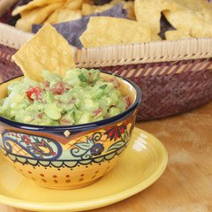 Bowl of guacamole dip with chips in the background.