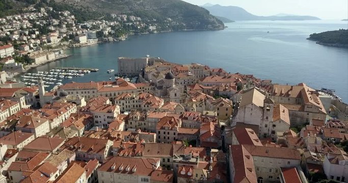 Aerial footage of Old Town in Dubrovnik, the camera passes over Dubrovnik Cathedral and Port showing the distant coastline