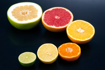 Fototapeta na wymiar cut pieces of different citrus fruits on dark background