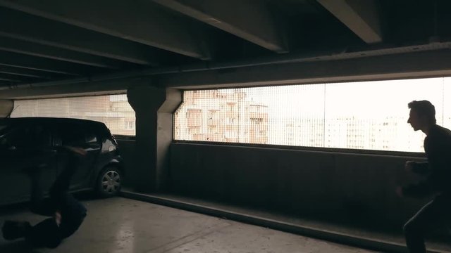 Man defends against an attacker with a knife. Assault in a parking garage. Criminal armed with a dagger attacks a man is is beaten back. Stunt men perform fight scene.